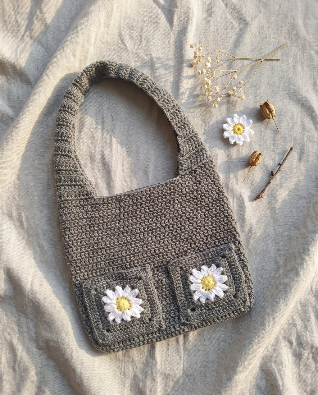 Crochet tote bag with daisy granny squares on a linen background with dried flowers