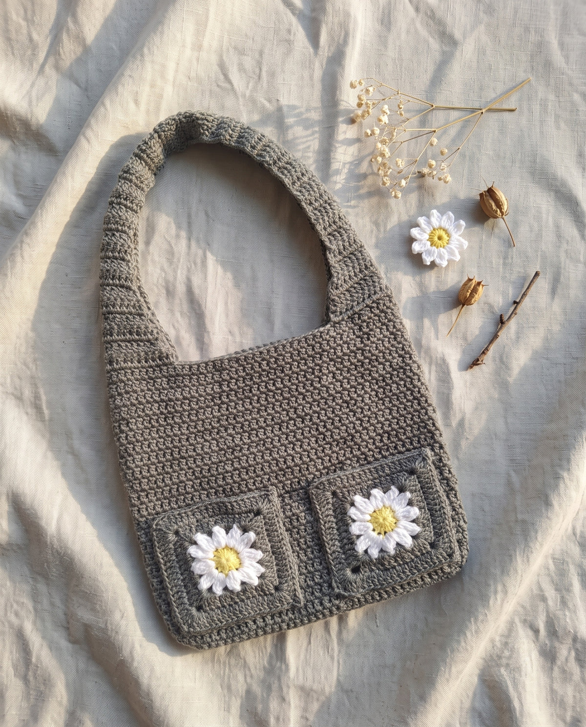 Crochet tote bag with daisy granny squares on a linen background with dried flowers