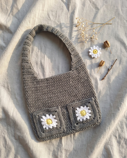 Crochet tote bag with daisy granny squares on a linen background with dried flowers