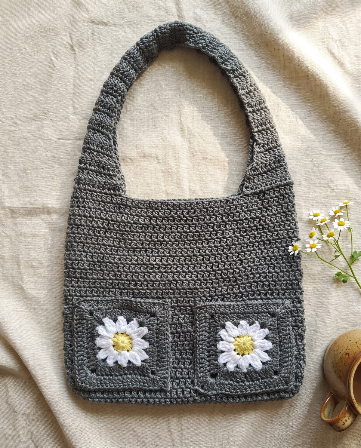 Grey crochet bag with daisy pocket detail styled with fresh chamomile flowers
