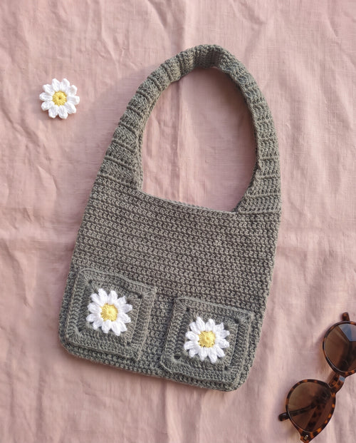 Handmade grey crochet shoulder bag with daisy pockets, flat lay with sunglasses